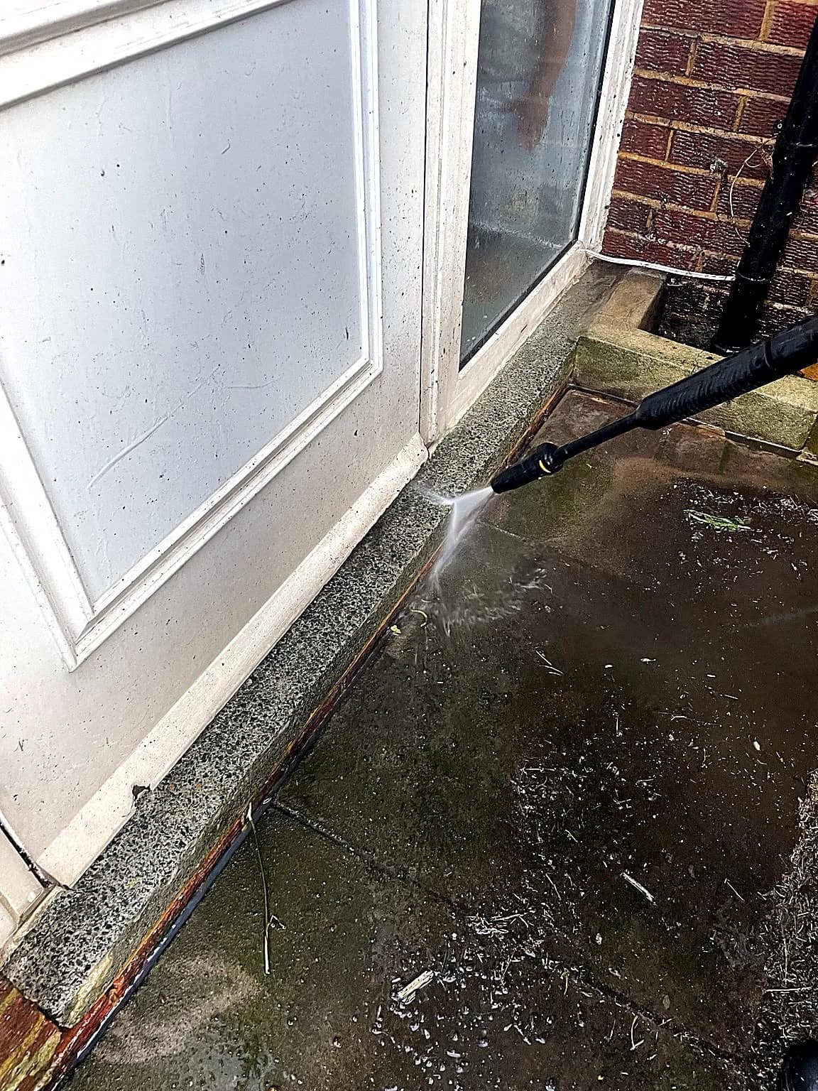 Pressure washing around a residential doorway and paved threshold.
