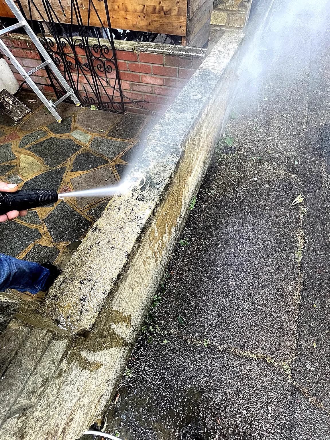 Pressure washing a low masonry boundary wall and adjoining paving.