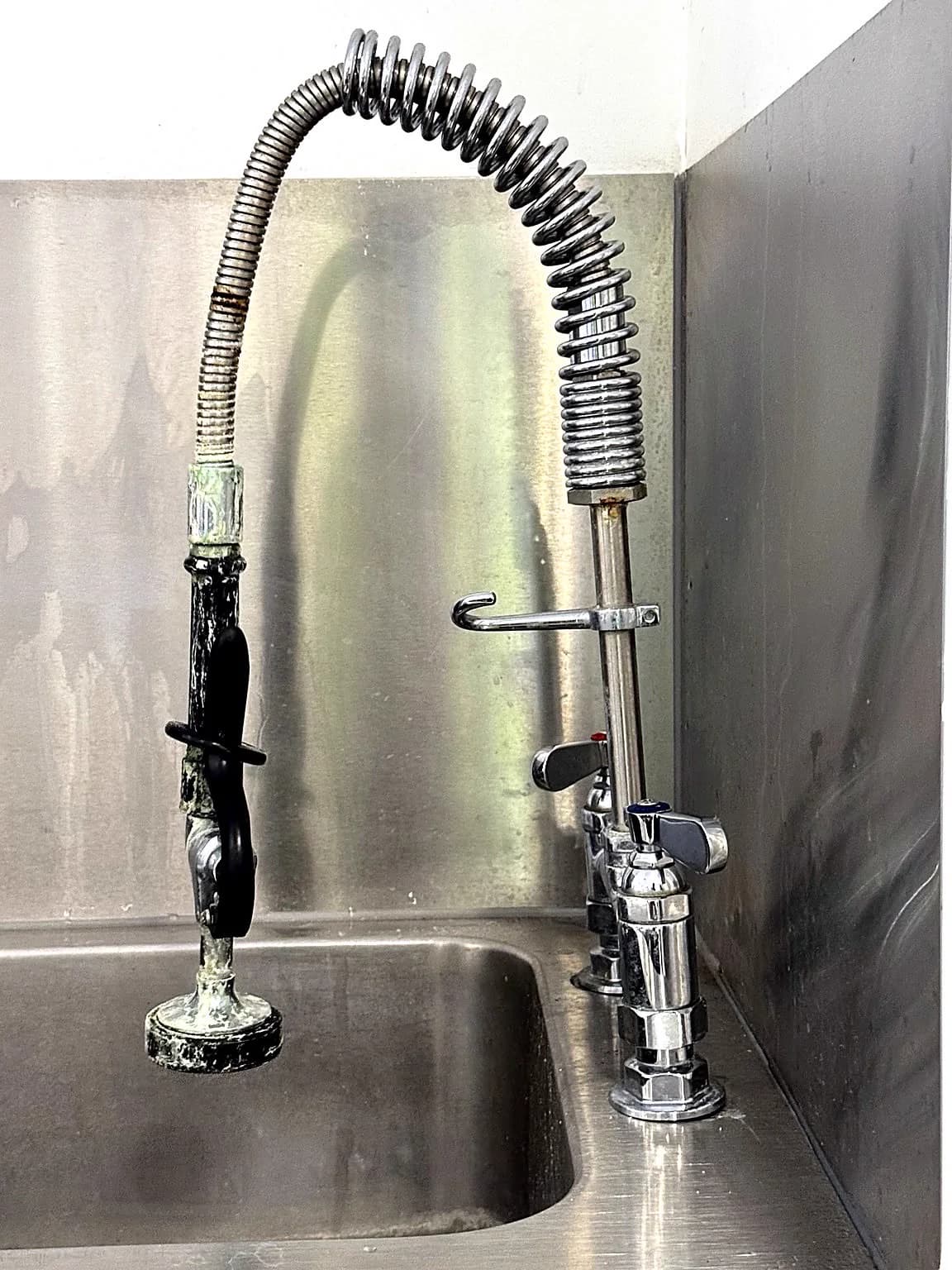 Flexible pre-rinse tap above a stainless-steel sink during maintenance.