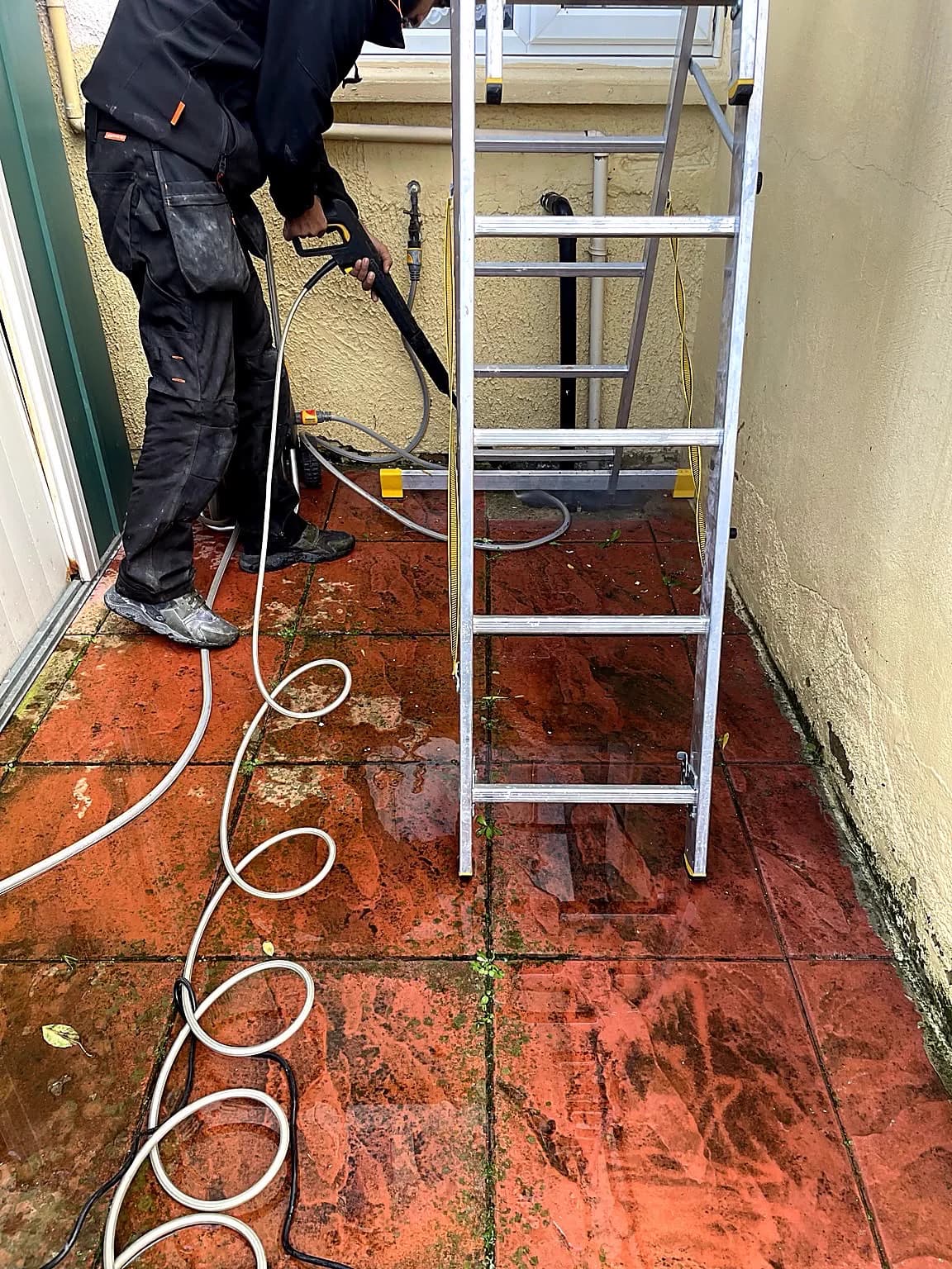 Operator pressure cleaning red paving in an enclosed outdoor area.