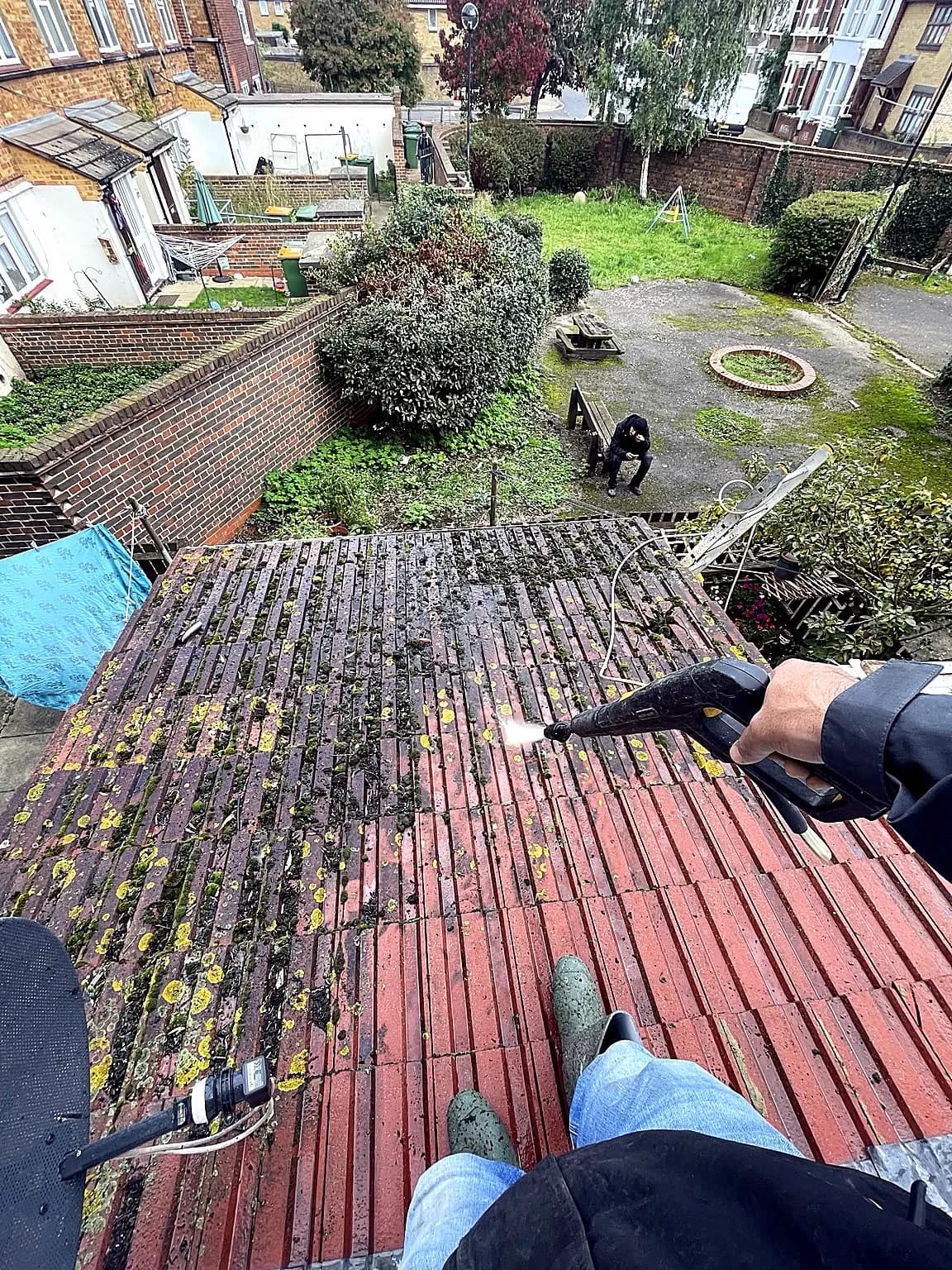 Pressure cleaning moss and debris from a tiled outbuilding roof.