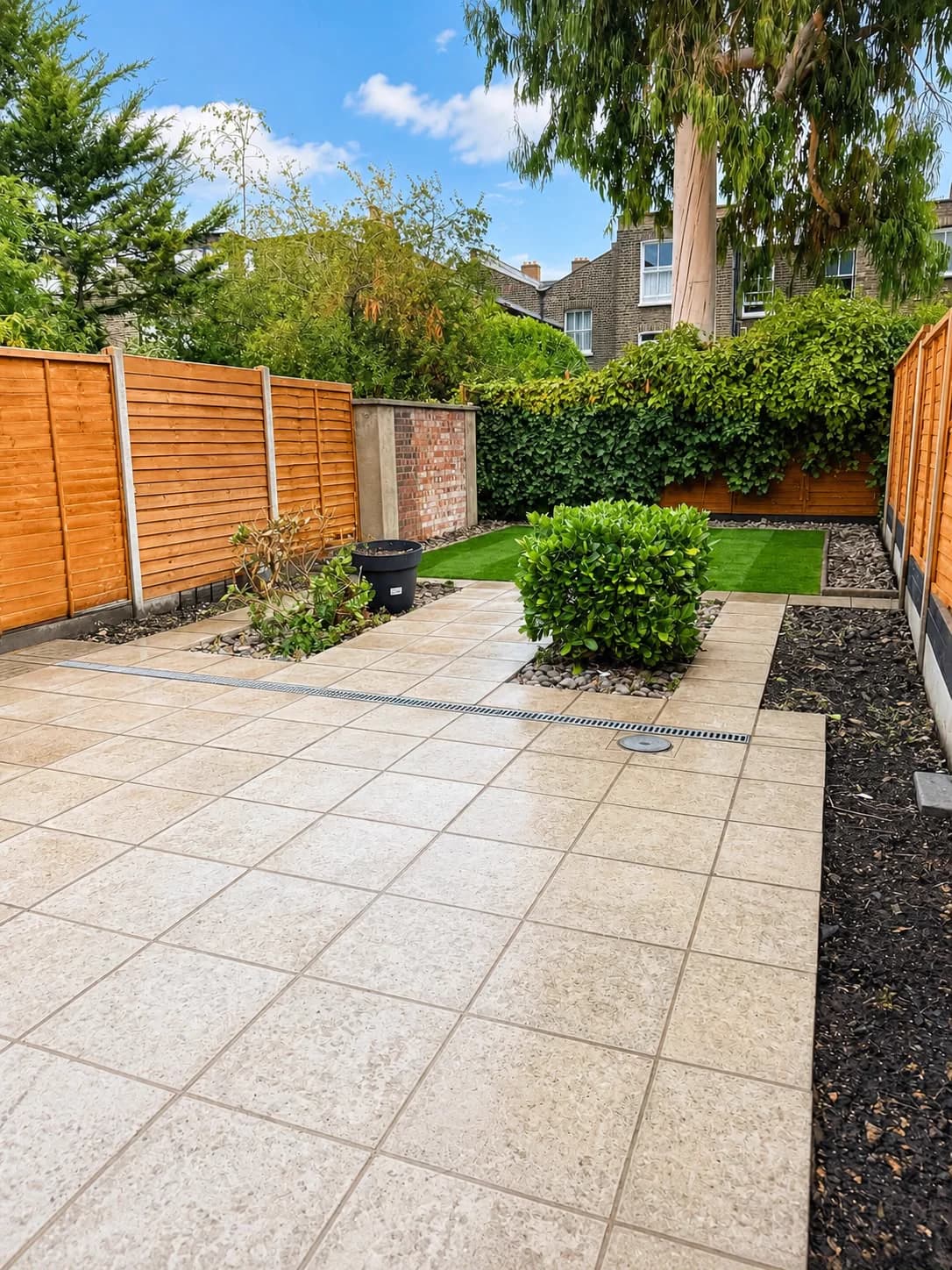 Paved rear garden with planted beds, timber fencing and a small lawn area.