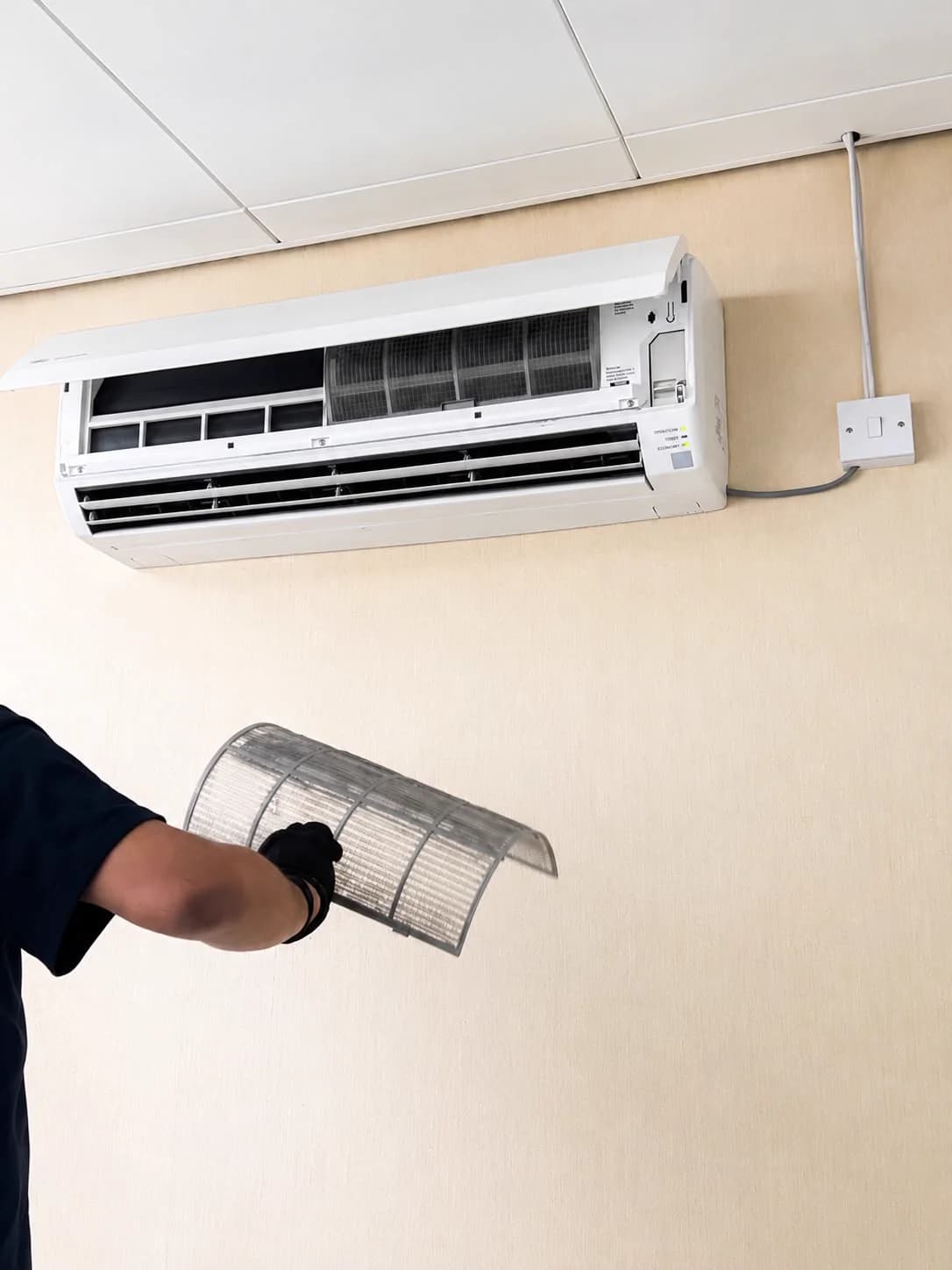 Technician removing the filter from a wall-mounted air-conditioning unit.