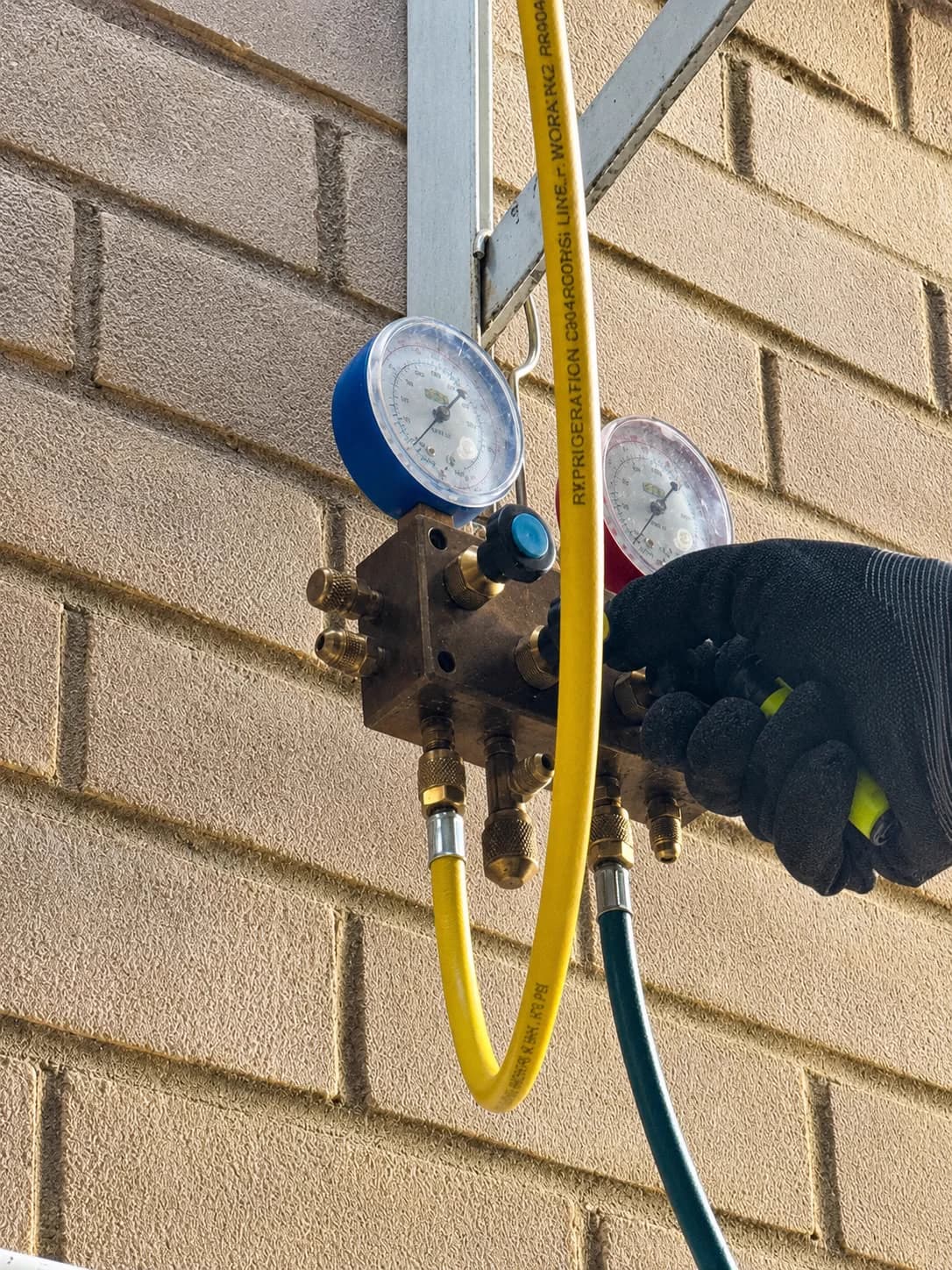 Technician using manifold gauges on an outdoor cooling system.