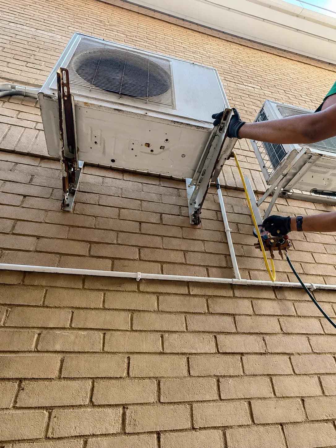 Technician servicing a wall-mounted outdoor air-conditioning unit.